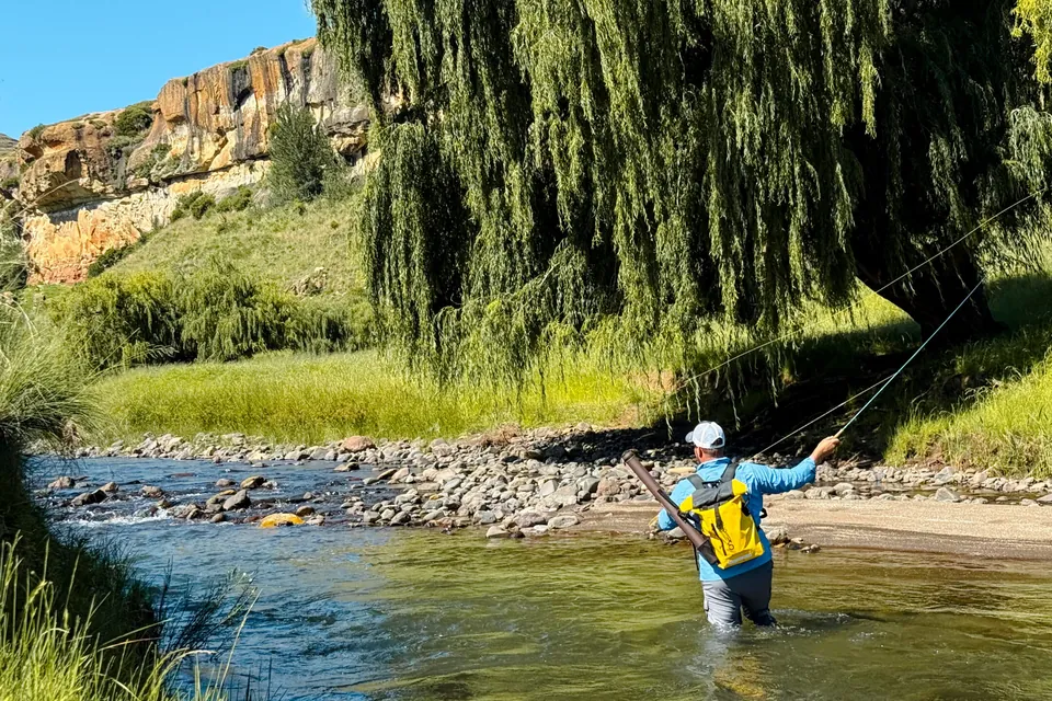 A fly fisherman casting in the river below the sandstone cliffs