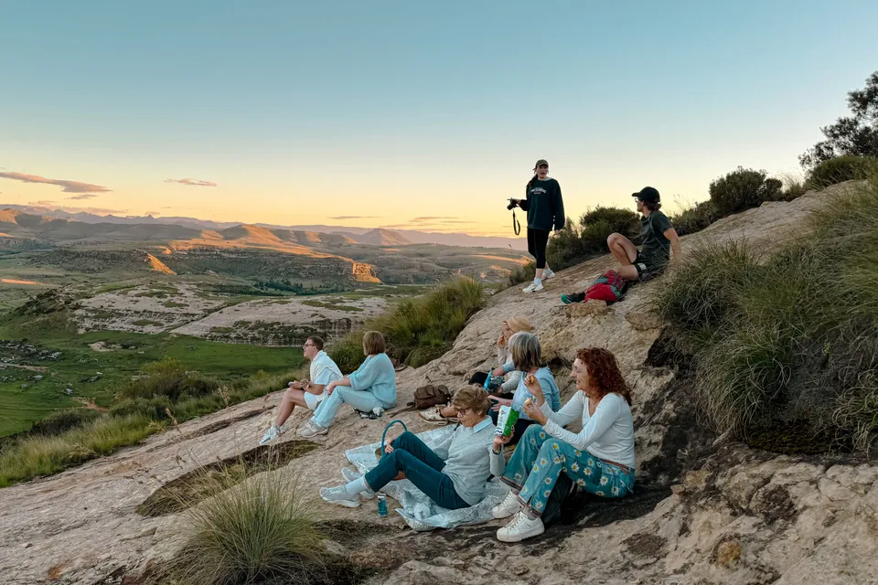 Friends sitting on a rocky outcrop watching the sun set over the valley