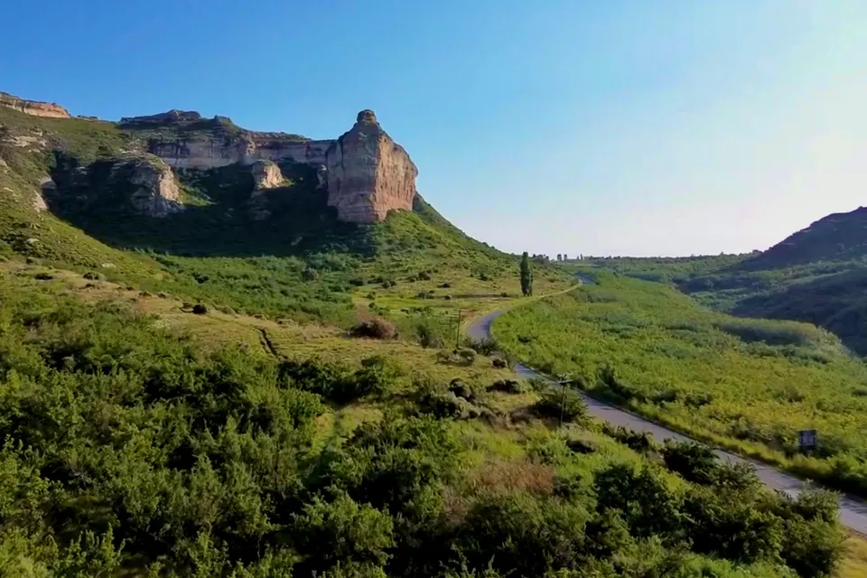 Sandstone cliffs above green foothills under a clear sky