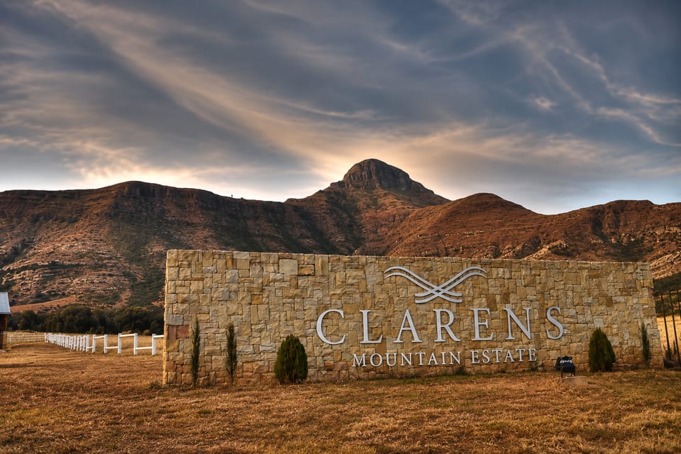 The sandstone entrance wall at Clarens Mountain Estate at dusk, with Mount Horeb rising behind it